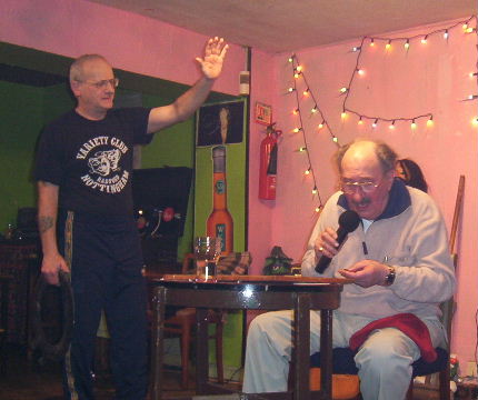 Gordon Cragg seated at bingo table, stareing intently at a bingo number while Oz attempts to attract his attention with hand up